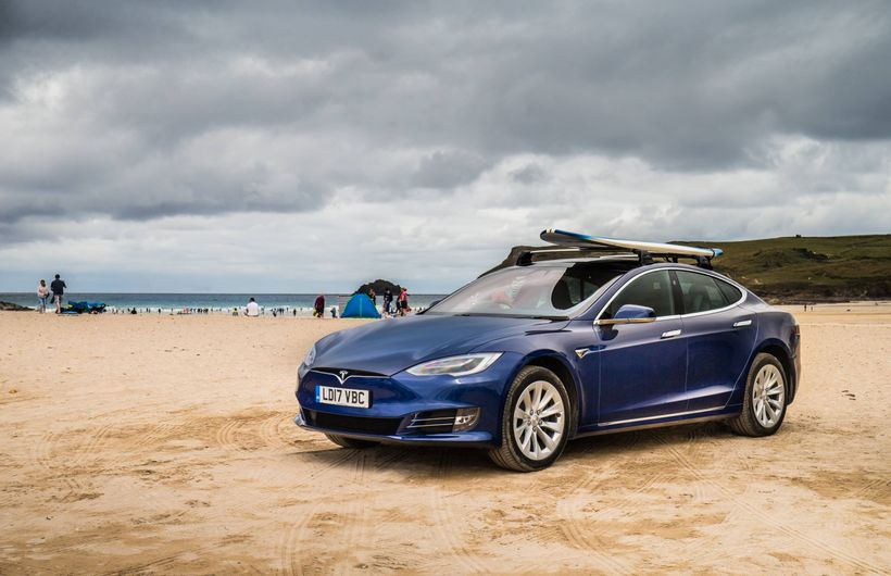 Blue Tesla Model S on beach with surfboard on roof